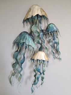 three blue and white jellyfish hanging from the ceiling in front of a gray wall