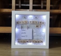 a white frame with words written on it and some lights in the background that read, will you be my godmother?