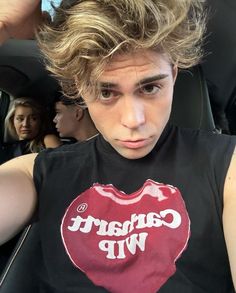 a young man sitting in the back seat of a car wearing a heart t - shirt