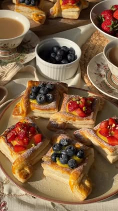 several pastries on a plate with berries and blueberries next to cups of tea