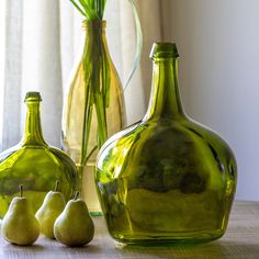 three green glass vases sitting on top of a table next to two pears