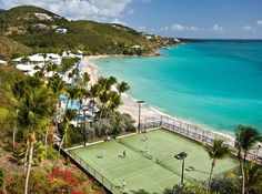 an aerial view of a tennis court on the beach with palm trees and blue water in the background