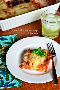 a white plate topped with lasagna next to a glass of water