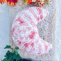 a pink and white knitted object sitting on top of a doily next to flowers