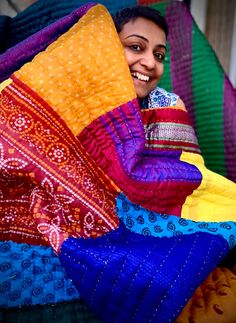 a woman sitting on top of a pile of colorful cloths and smiling at the camera