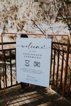 a welcome sign hanging from a metal fence next to a body of water with trees in the background