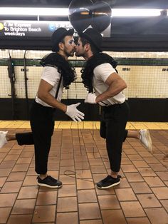 two men dressed in black and white are kissing each other on the subway platform,