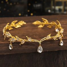 a gold bracelet with crystal stones and leaves on the side, sitting on top of a wooden