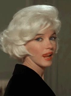 a woman with white hair wearing a black dress and red lipstick on her lips is looking at the camera