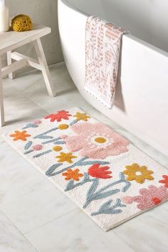 a bathroom rug with flowers on it next to a bathtub and toilet in the background