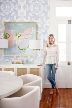 a woman standing next to a table in a room with blue and white wallpaper