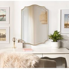 a white desk topped with a mirror next to a wall filled with pictures and plants