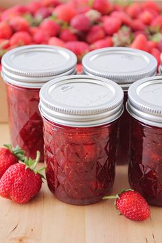 four jars of strawberry jam with strawberries in the background