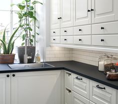 a kitchen with white cabinets and black counter tops is pictured in this image, there are potted plants on the window sill