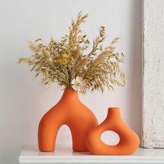 two orange vases sitting on top of a white shelf