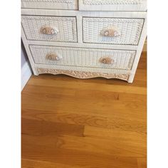 a white wicker dresser with drawers and knobs on the top drawer, sitting on a hard wood floor