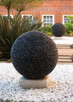 a large black ball sitting on top of a white stone slab in front of a building