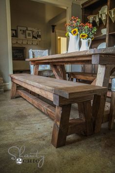 a wooden bench sitting next to a table in a living room with flowers on it