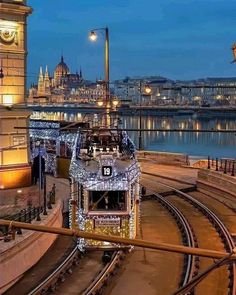 a train traveling down tracks next to a tall building with lights on it's sides