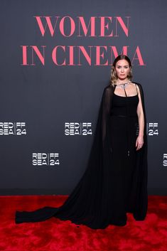 a woman in a black dress standing on a red carpet with her cape over her shoulders