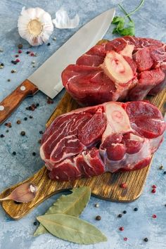 two pieces of raw meat on a cutting board next to a knife and peppercorst