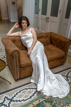 a woman in a white dress sitting on a brown couch next to a coffee table