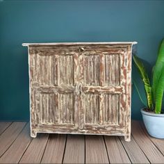 an old wooden cabinet next to a potted plant on a wood floor with blue walls in the background