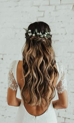 a woman with long curly hair wearing a white dress and flower crown in her hair