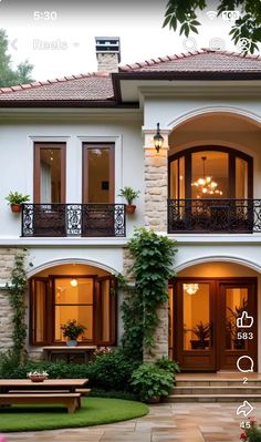 a large white house with lots of windows and plants on the front porch, surrounded by greenery