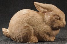 a wooden sculpture of a rabbit sitting on top of a gray carpeted floor next to a black wall