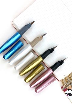 several pens are lined up in a row on top of a notepad, next to an open notebook