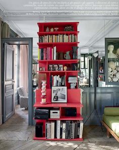 a red book shelf filled with books in a living room next to a green couch