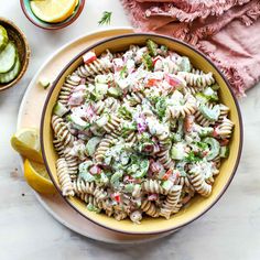 a bowl filled with pasta salad next to sliced cucumbers and lemon wedges