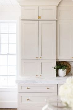 a kitchen with white cabinets and marble counter tops in the center, along with a potted plant