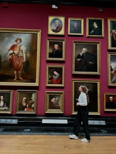 a woman is walking in front of many paintings