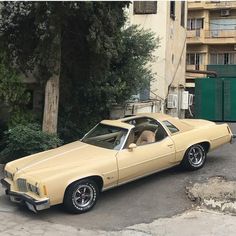 a tan car parked in front of a tall building