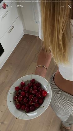 a woman is holding a bowl of cherries