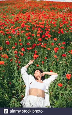 a woman laying in the middle of a field of red flowers with her hands behind her head