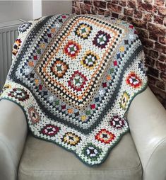 a crocheted granny's afghan sits on a chair in front of a brick wall