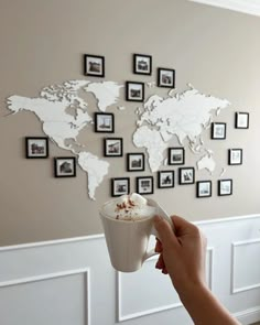 a person holding a coffee cup in front of a world map on the wall with black and white frames