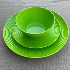 three green plates and two cups on a gray tablecloth with a white cloth in the background