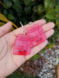 a pair of pink earrings sitting on top of a persons hand in front of some plants