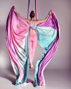 a woman is doing aerial acrobatics on a pole with pink and blue fabric