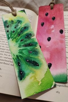 two bookmarks with watercolor designs on them sitting on top of an open book