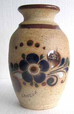 a ceramic vase with flowers painted on the front and sides, sitting against a white background