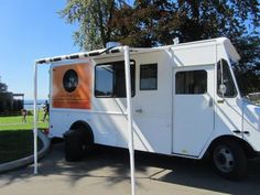 an orange and white food truck is parked on the side of the road near some trees