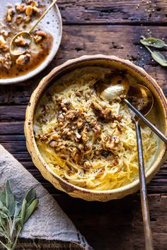 two bowls filled with pasta and meat on top of a wooden table next to spoons