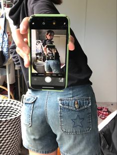 a person taking a selfie with their cell phone while wearing shorts and a black t - shirt