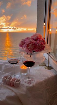 two glasses of wine are sitting on a table with flowers and candles in front of the ocean