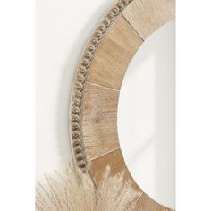 a decorative mirror hanging on the wall next to a white wall and some dried grass